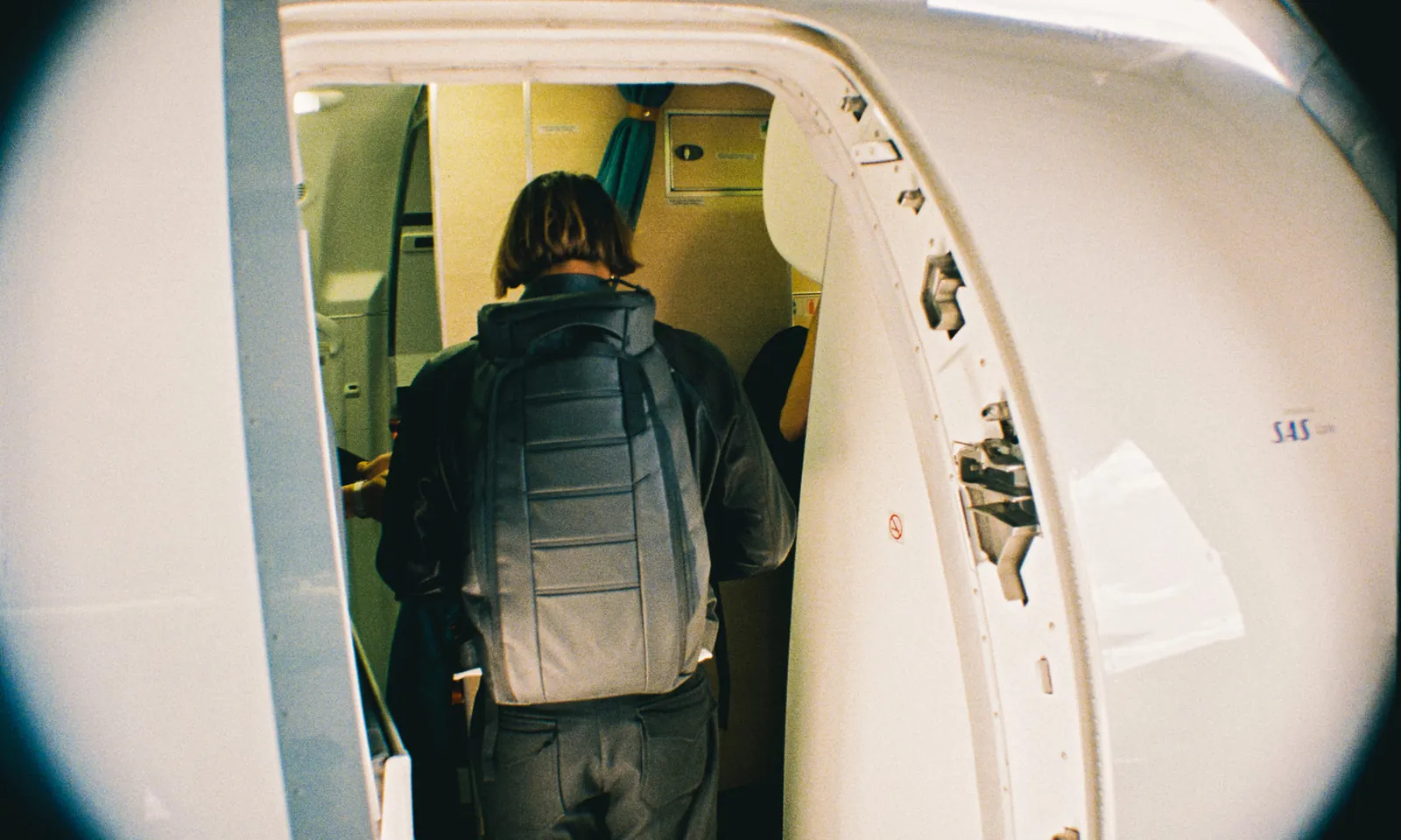 A backpack fits under an airplane seat while a purse rests on the chair.