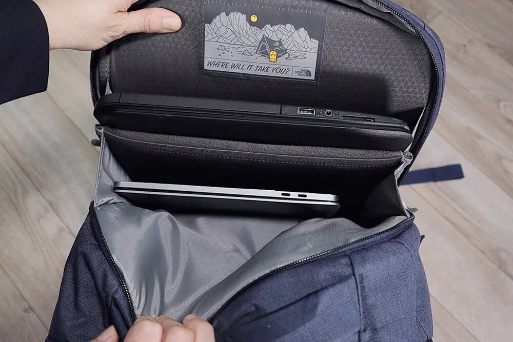 A professional backpack designed to hold two laptops sits on a wooden table.