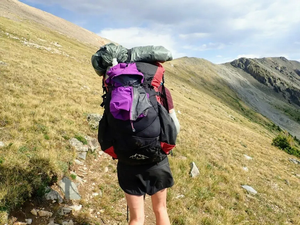 Hands tightening the side straps of a hiking backpack to prepare for travel.