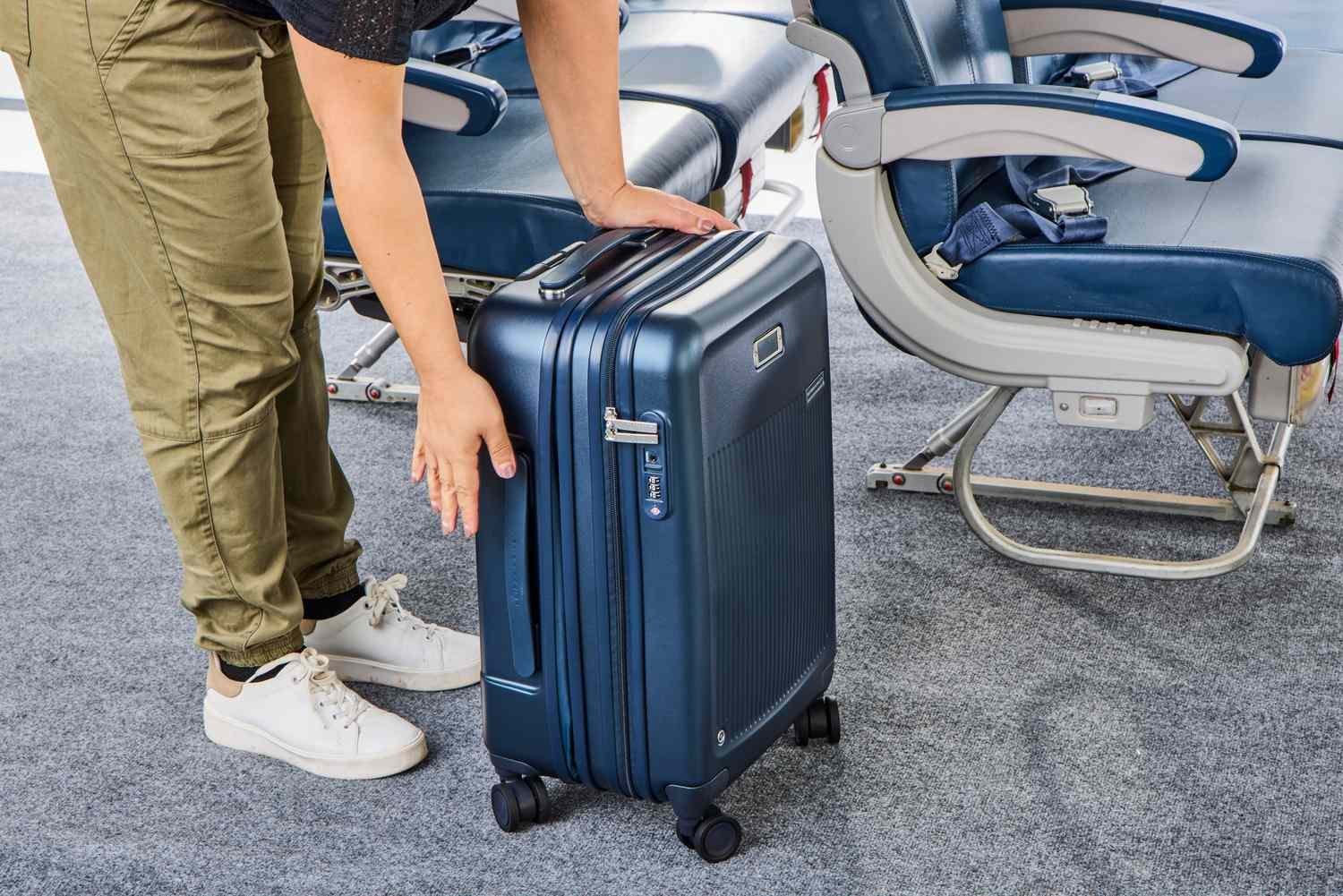 Traveler attempting to fit a large suitcase into a small airplane overhead bin.