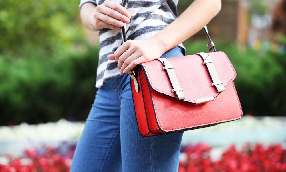 A woman wearing a stylish sling bag while walking down a sunny city street.