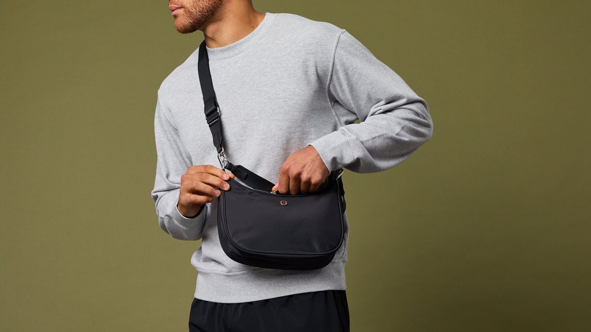 A small sling purse shown next to a large laptop to illustrate capacity.