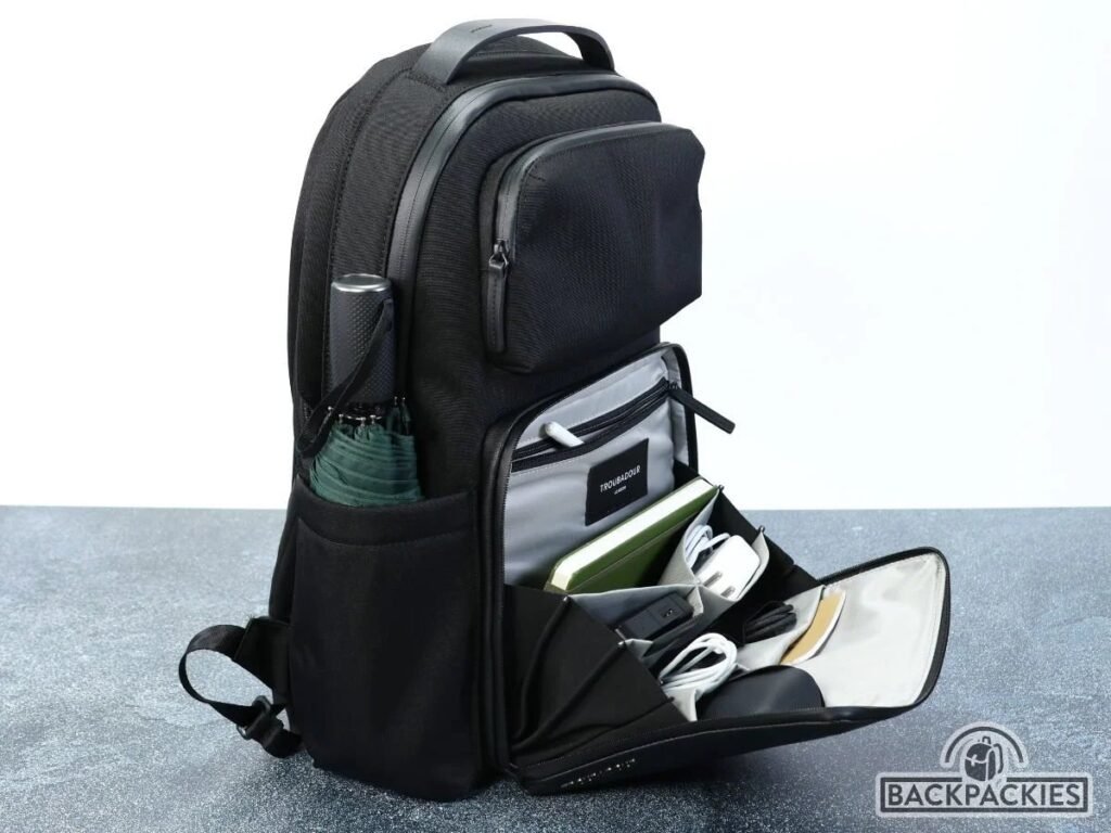 A premium professional business backpack sits on a modern wooden bench in an office.