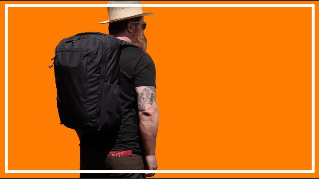 A sleek travel backpack stands on a concrete floor inside a bright airport.