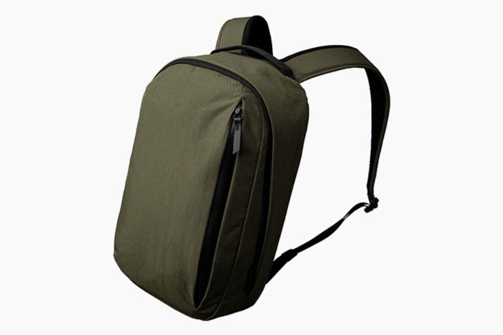 A small dark olive canvas backpack resting on a weathered wooden park bench.