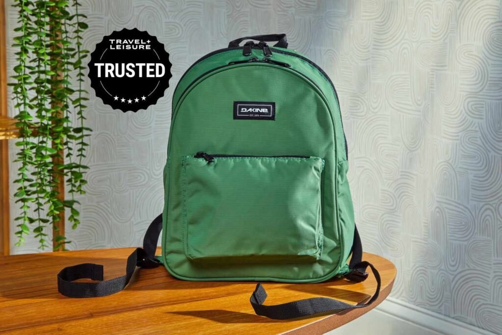 A stylish compact backpack sits on a wooden bench in a sunlit park.